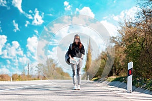 A young woman walks along the road with a map in her hands. Outdoor. Concept of hitchhiking and local travel