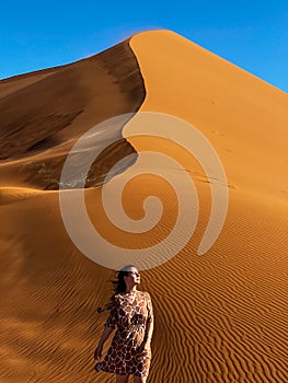 A young woman walks along sandy dunes in Namibia. Dune 45 or 17 at sunset.