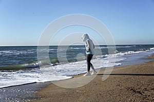 A young woman walks along the sandy seashore in the winter season on a sunny day. Holidays at the resort in the off-season