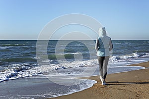 A young woman walks along the sandy seashore in the winter season on a sunny day. Holidays at the resort in the off-season