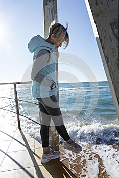 A young woman walks along the seashore on a sunny day in the low season. Blonde in a birch jacket and jeans. Calm and relaxation.