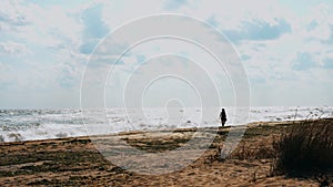 Young woman walks along windy wavy beach as wind blows through her hair