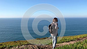 A young woman walks away from the camera on a hill. The ocean on a background.