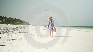 Young woman walks barefoot on beach along ocean