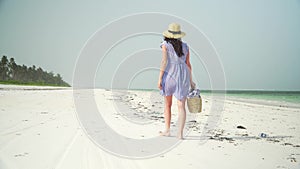 Young woman walks barefoot on beach along ocean