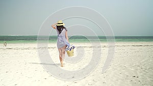 Young woman walks barefoot on beach towards ocean
