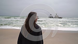 Young woman walks at the beach near sunken trawler, shipwreck. Old ship Zeila.