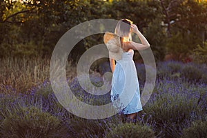 Young Woman Walks Outside City Among Lavender. Girl Stands at Sunset on Meadow and Looks Back