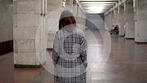 A young woman walks in the subway. A girl in a coat and glasses