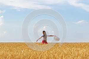 Young woman walks through wheat field with hat in hands and enjoying Sunny day. Freedom and rest