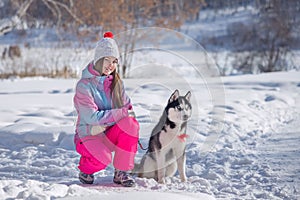 A young woman walks in the winter forest with her pet. friend of the dog with blue eyes, husky, Siberian