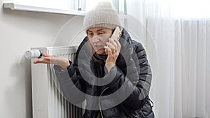 Young woman in warm clothes speaking to tecnician by phone about broken heater or radiator photo