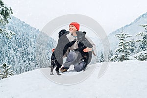 A young woman in warm clothes walking her 2 dogs in a picturesque snowy mountain outdoor. Female laughing and playing with pets