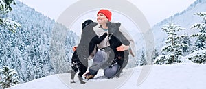 A young woman in warm clothes walking her 2 dogs in a picturesque snowy mountain outdoor. Female laughing and playing with pets