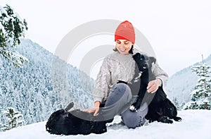A young woman in warm clothes walking her 2 dogs in snowy mountain outdoor. Female laughing, hugging, and playing with pets. Human
