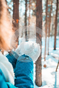 Young woman in warm mittens hold snow in the winter forest. Winter nature. Selective focus