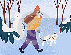 Young woman in warm outerwear walking dog in park and looking in smartphone. Female character with pet in winter forest