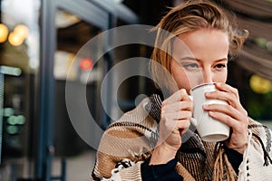 Young woman in warm plaid drinking hot tea while stanging outdoors photo