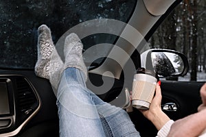 Young woman in warm socks with coffee resting inside car