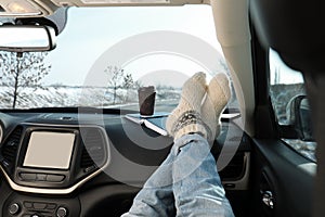 Young woman in warm socks holding her legs on car dashboard