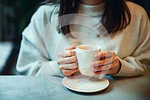 Young woman in warm sweater holding cup of coffee and planing personal goals for new year.