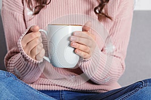 Young woman in warm sweater holding cup of hot drink