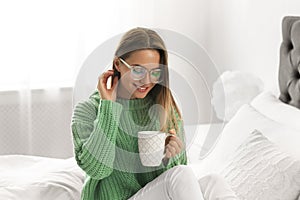 Young woman in warm sweater with hot drink on bed