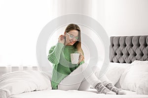 Young woman in warm sweater with hot drink on bed