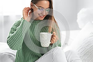 Young woman in warm sweater with hot drink on bed