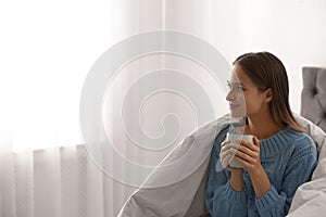 Young woman in warm sweater with hot drink on bed. Space for text photo