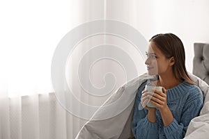 Young woman in warm sweater with hot drink on bed. Space for text