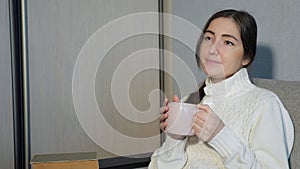 Young woman in warm sweater sitting on sofa and and drinking tea at home