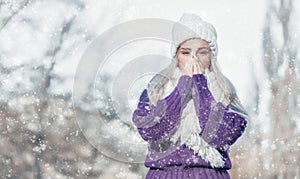 Young woman warming her hands, wearing warm clothing on snowing winter day outdoors. Cute girl feeling cold. Winter concept