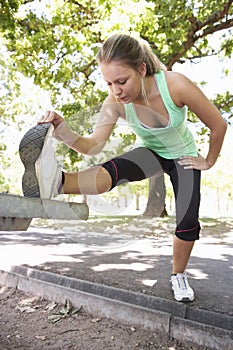 Young Woman Warming Up With Stretches On Park Bench