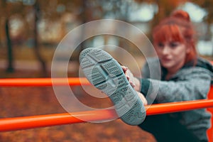 Young woman warming up and stretching her leg on bar in park at autumn, focus on shoe