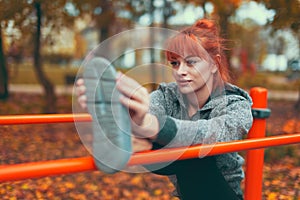 Young woman warming up and stretching her leg on bar in park at autumn, selective focus