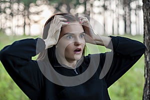 Young woman was afraid and put her hands on her head. girl is shocked and holds her head. outdoors