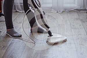 A young woman washes the floor with a modern steam cleaner.