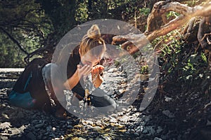 Young woman washes her face from mountain river. Tourism Adventure Bushcraft Survival Scout Concept