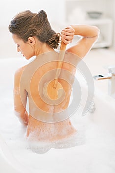 Young woman washing with body brush in bathtub