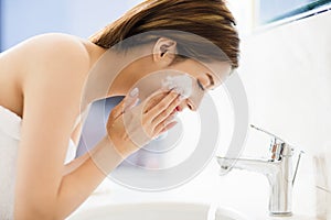 Woman washing face with clean water in bathroom