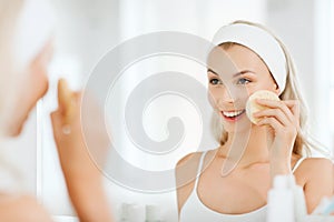 Young woman washing face with sponge at bathroom photo