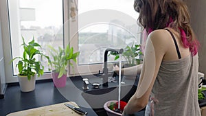 Young woman washing fresh salad ingredients in a sink
