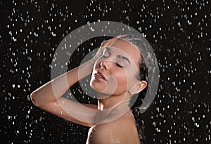 Young woman washing hair while taking shower on black background