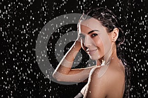 Young woman washing hair while taking shower on black background