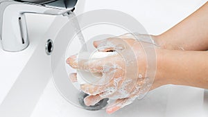 Young woman washing hands under streaming water from faucet with soap in bathroom, hygiene concept