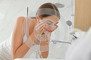 Young woman washing her face with water in bathroom