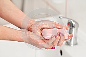 Young woman washing her hands under water tap faucet with pink soap bar. Detail on fingers, nails covered purple polish. Personal