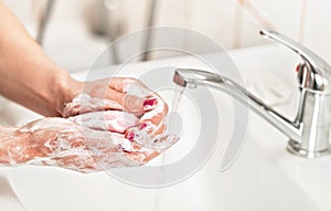 Young woman washing her hands under water tap faucet with pink soap bar. Detail on suds covered skin. Personal hygiene concept -