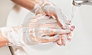 Young woman washing her hands under water tap faucet with soap. Detail on fingers, nails covered purple polish. Personal hygiene